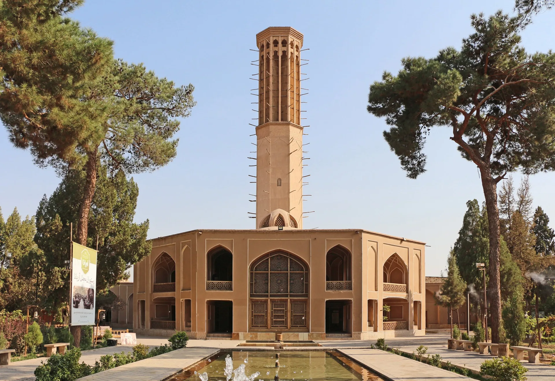 باغ دولت‌آباد در یزد: کوشکی خشتی با بادگیری بسیار بلند، احاطه‌شده با درختان کاج و با حوضی در پیش‌زمینه